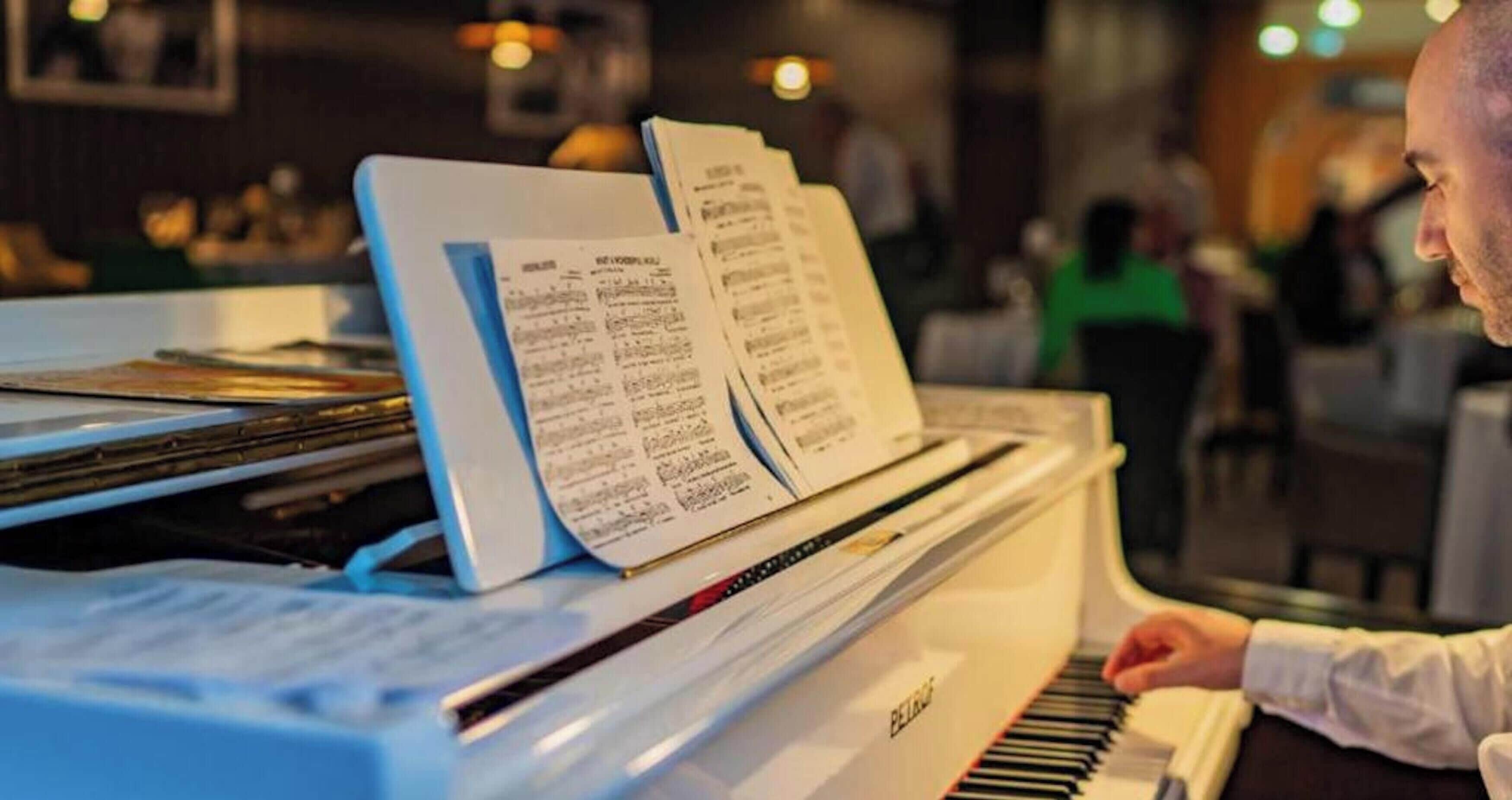 A piano with sheet music on it, in a room with tables and chairs.