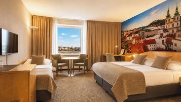 A hotel room with a large bed, a desk, a chair, a TV, and a window with a cityscape view.