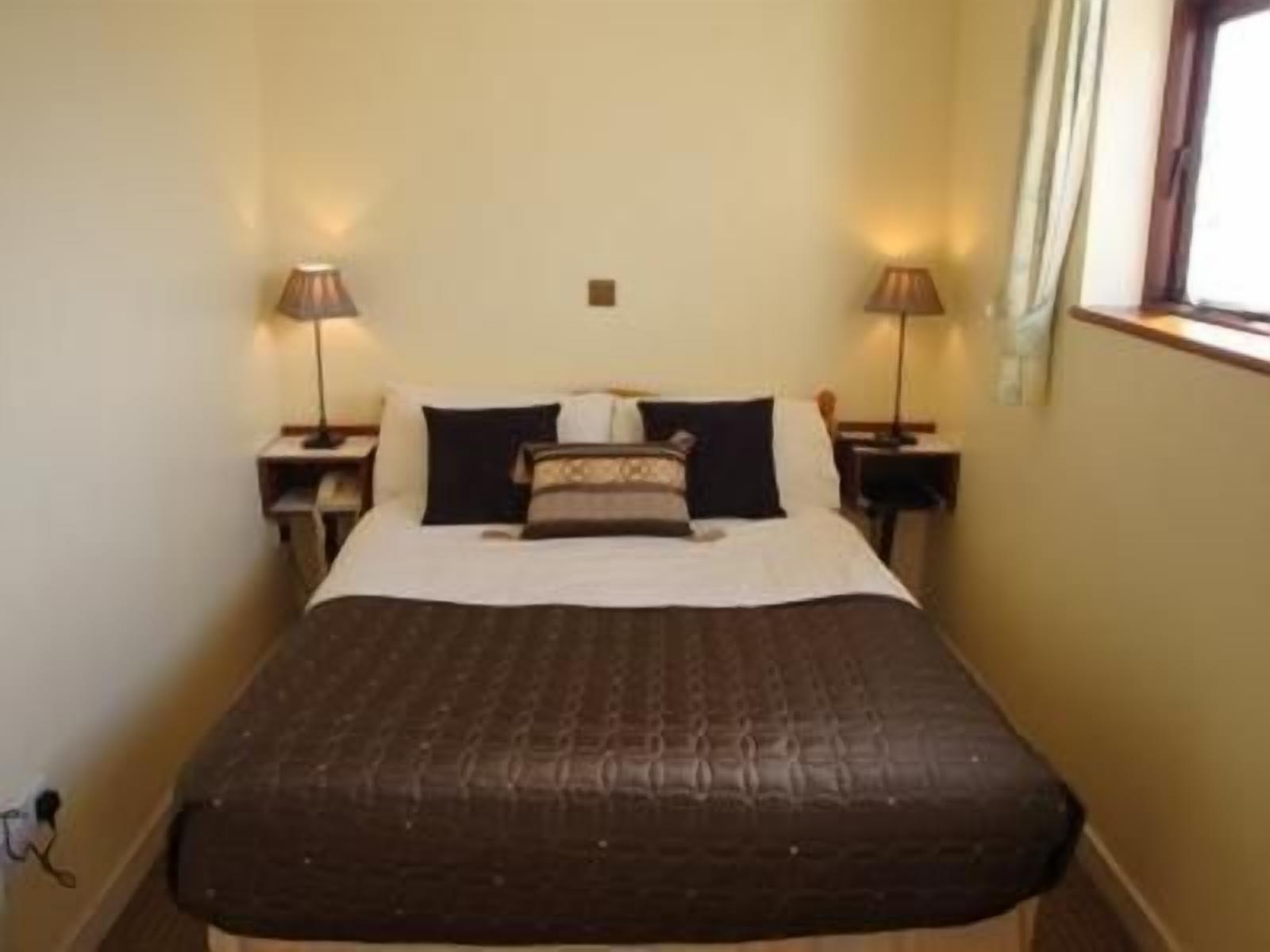 Una habitación estándar de hotel con una cama individual, dos mesitas de noche con lámparas y una ventana con cortinas.