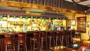 Una zona de bar con sillas de madera, una barra y diferentes botellas y vasos.