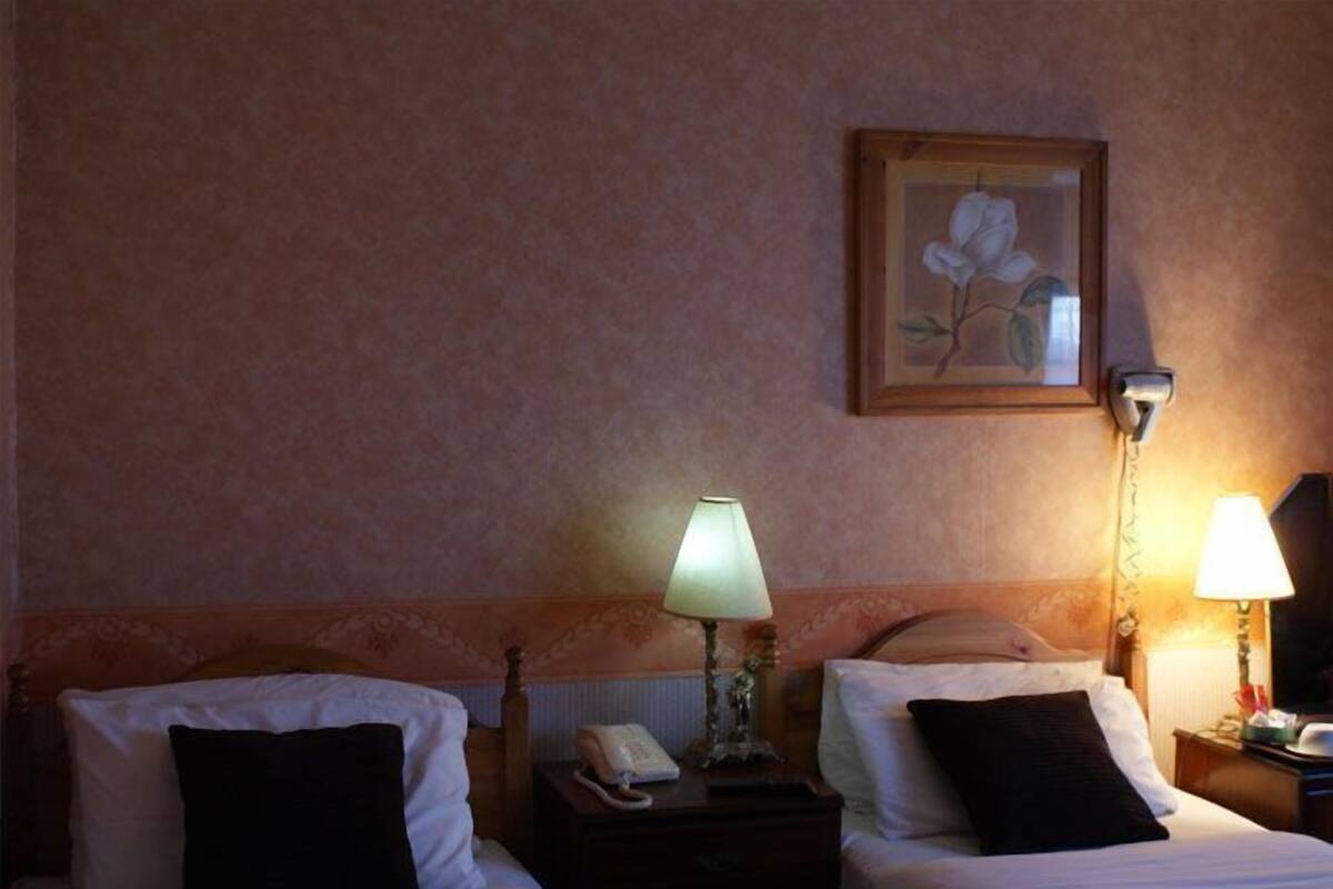 A hotel room with two beds, a nightstand with a lamp, a telephone, and a framed picture on the wall.