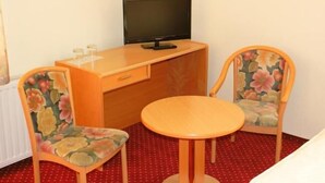 Ein kleines Zimmer mit einem Holztisch, zwei Stühlen mit floralem Bezug, einem Fernseher und einem kleinen runden Tisch.