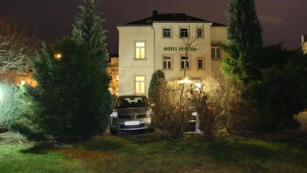 Ein Hotel namens „HOTEL PENSION“ mit einem geparkten Auto davor, umgeben von Bäumen und Sträuchern.