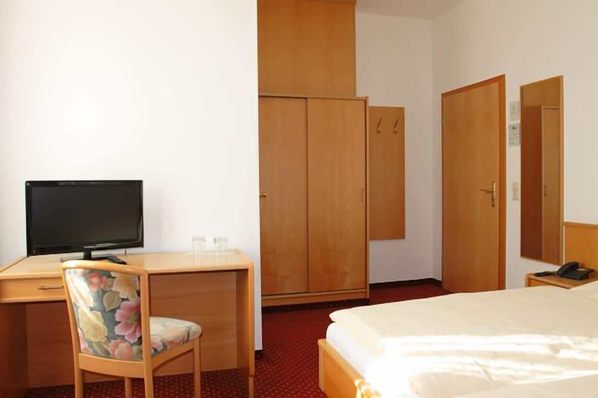 A hotel room with a bed, a desk with a computer, a chair, and wooden wardrobes.