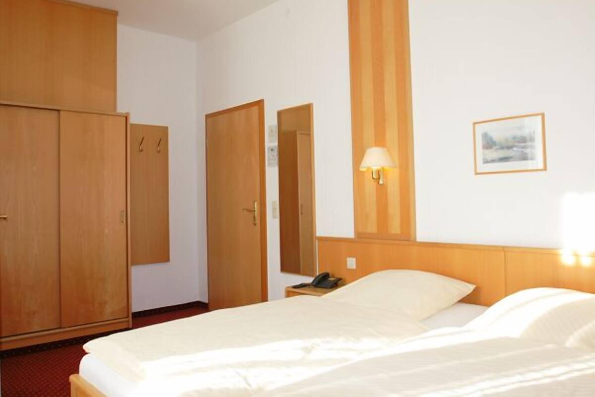 A hotel room with a bed, a wardrobe, a mirror, a nightstand, and a wall-mounted lamp.