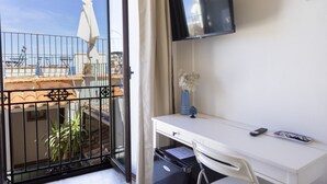 Un balcón con vistas al mar, un escritorio blanco con un televisor, un florero con flores y una silla.