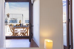 A view from inside a room to an outdoor patio area with a table and chairs, a railing, and a view of the sky. - Dolce Vita Rooms and Apartments  (Cefalù)