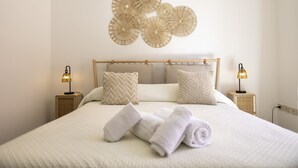 Una cama bien hecha con toallas enrolladas, dos lámparas de noche y una obra de arte en la pared superior.