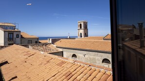 Un pueblo costero con tejados de tejas rojas y una torre destacada, con el mar al fondo.