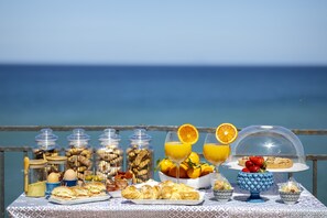 A breakfast buffet with various food items and drinks on a table with a view of the sea. - Dolce Vita Rooms and Apartments  (Cefalù)