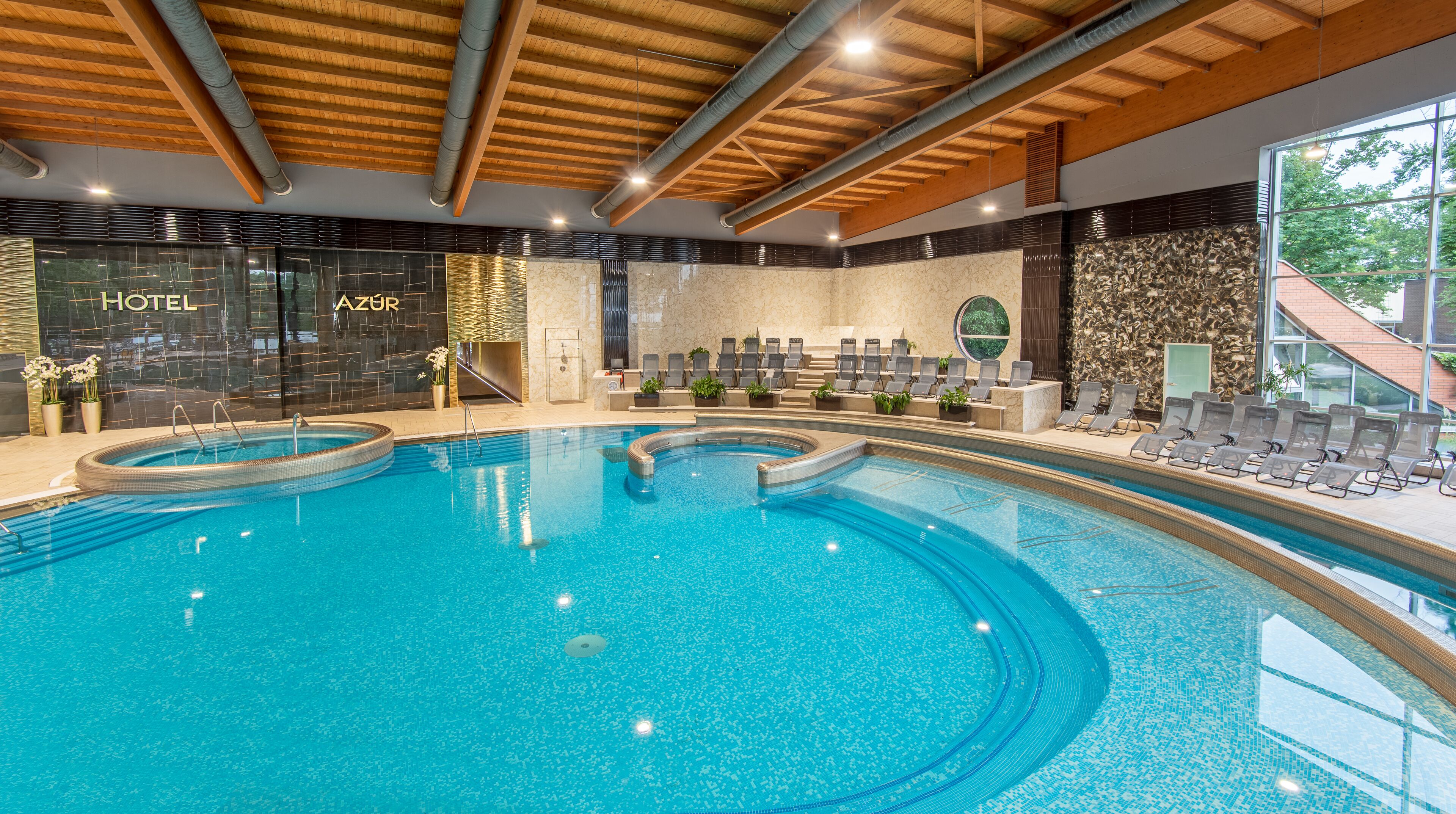 Un hôtel moderne avec un intérieur élégant, une grande piscine intérieure, des chaises longues et un espace de réception.