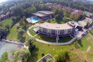 An aerial view of a campus with a central circular building, a swimming pool, and surrounding greenery. - Hotel Azúr (Siófok)