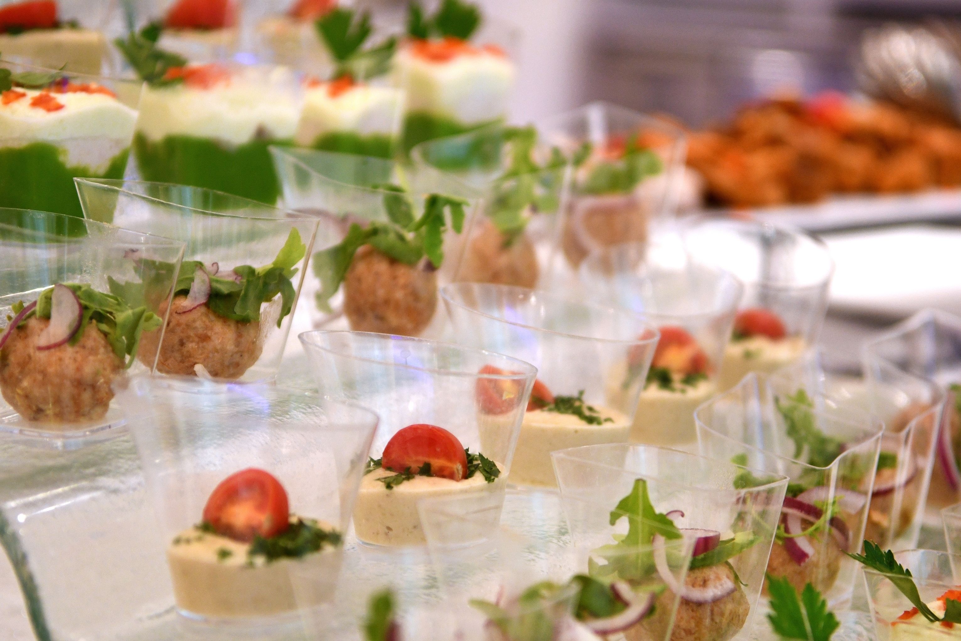A variety of appetizers arranged in clear glasses, some with meatballs and garnishes like tomatoes and herbs.