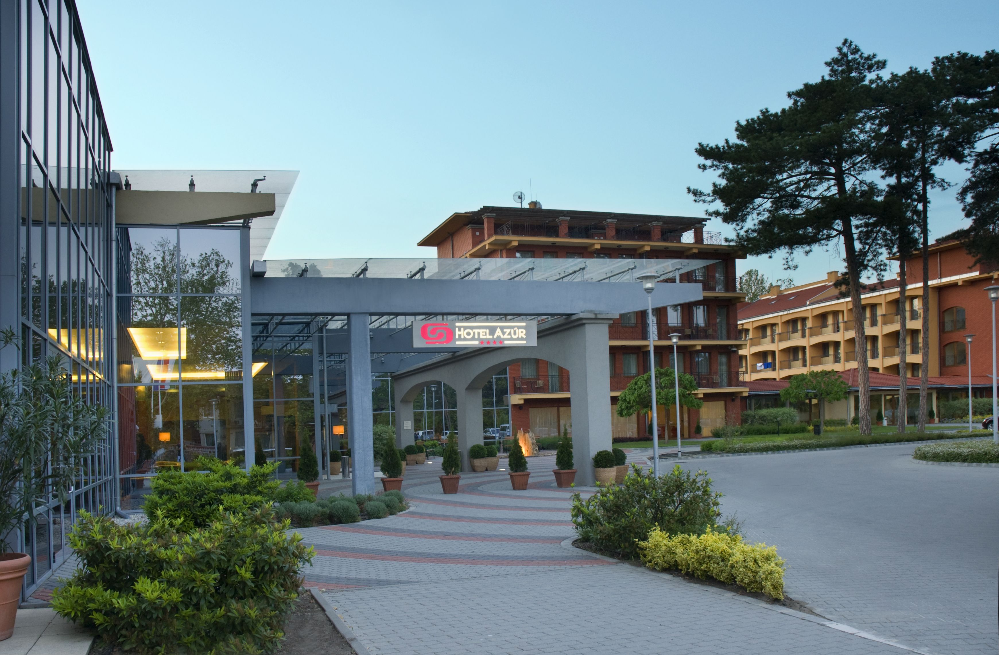 Entrada de un hotel con fachada de vidrio, un paseo techado y un cartel que dice 'HOTEL AZUR'.
