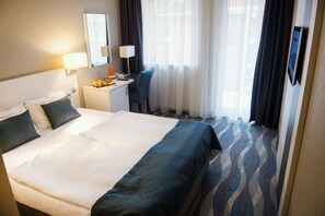 A hotel room with a large bed, a desk with a computer, a chair, and a window with curtains. - Hotel Azúr (Siófok)