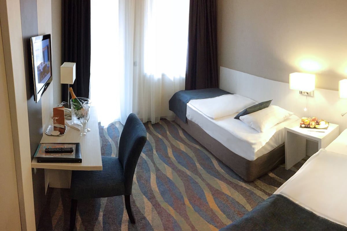 Quarto de hotel com cama, escrivaninha, cadeira, televisão e luminária.