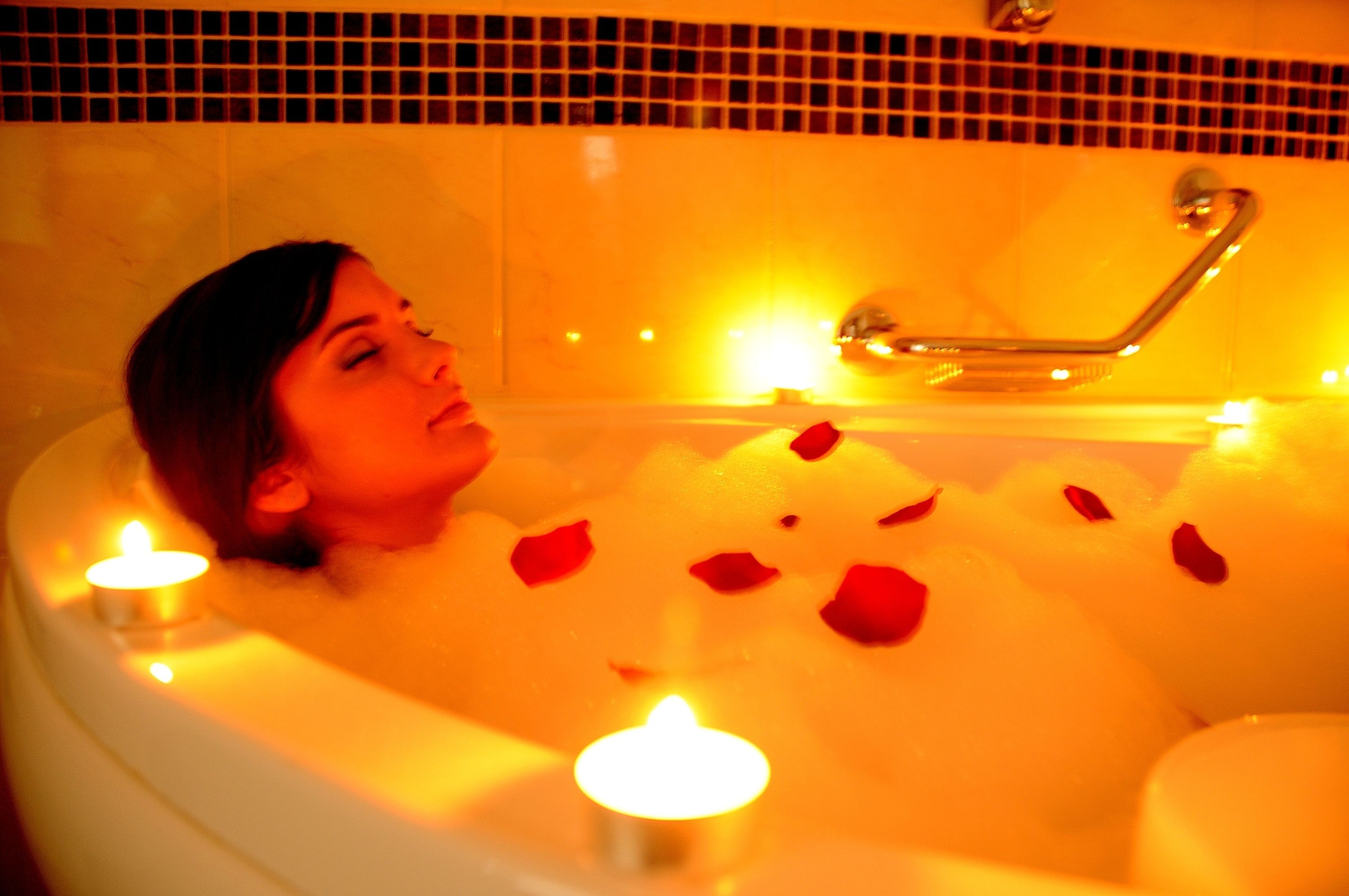Une personne dans une baignoire, entourée de pétales de rose et de bougies.