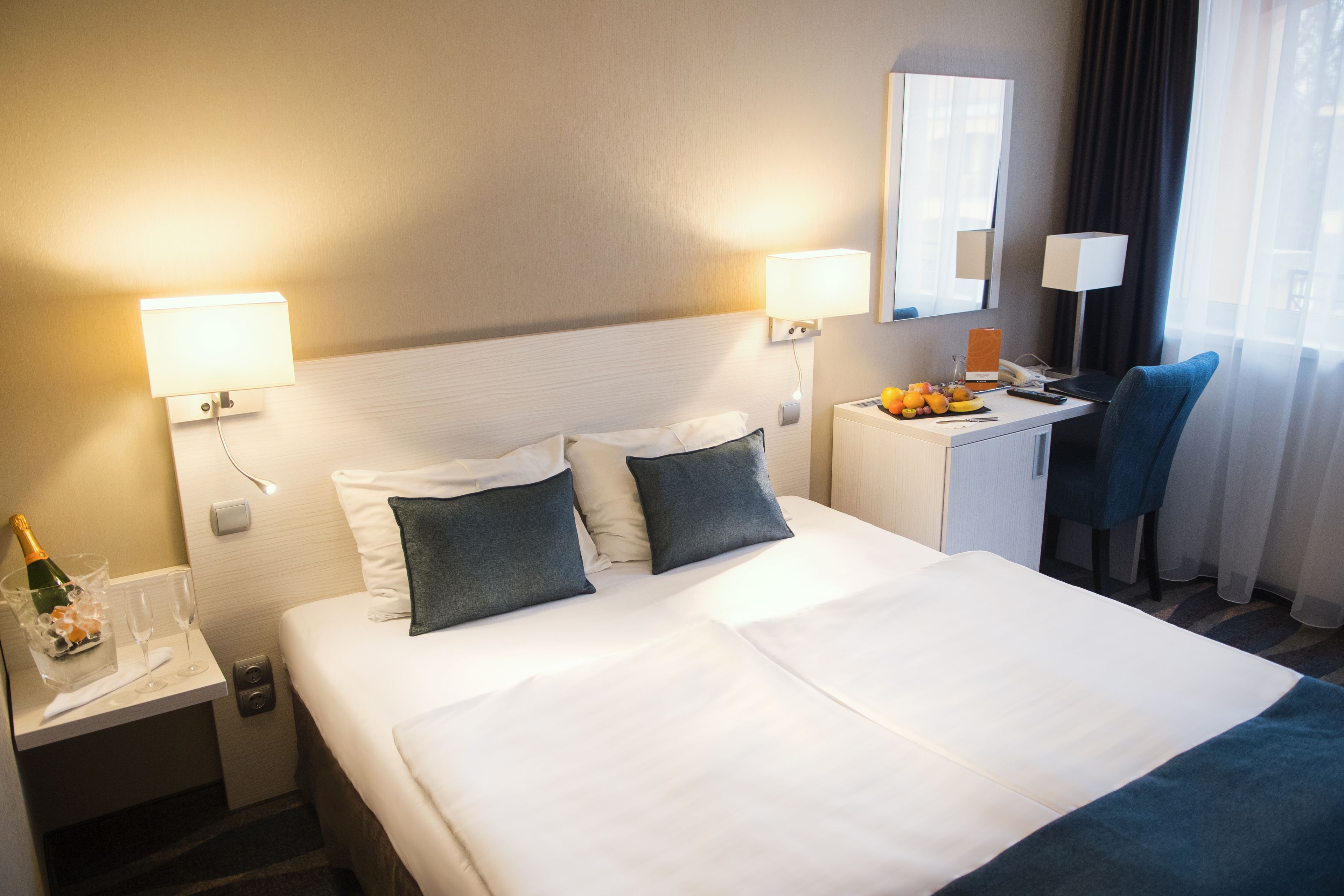 Una habitación de hotel con una cama bien hecha, un escritorio con una lámpara, una silla y un frutero.
