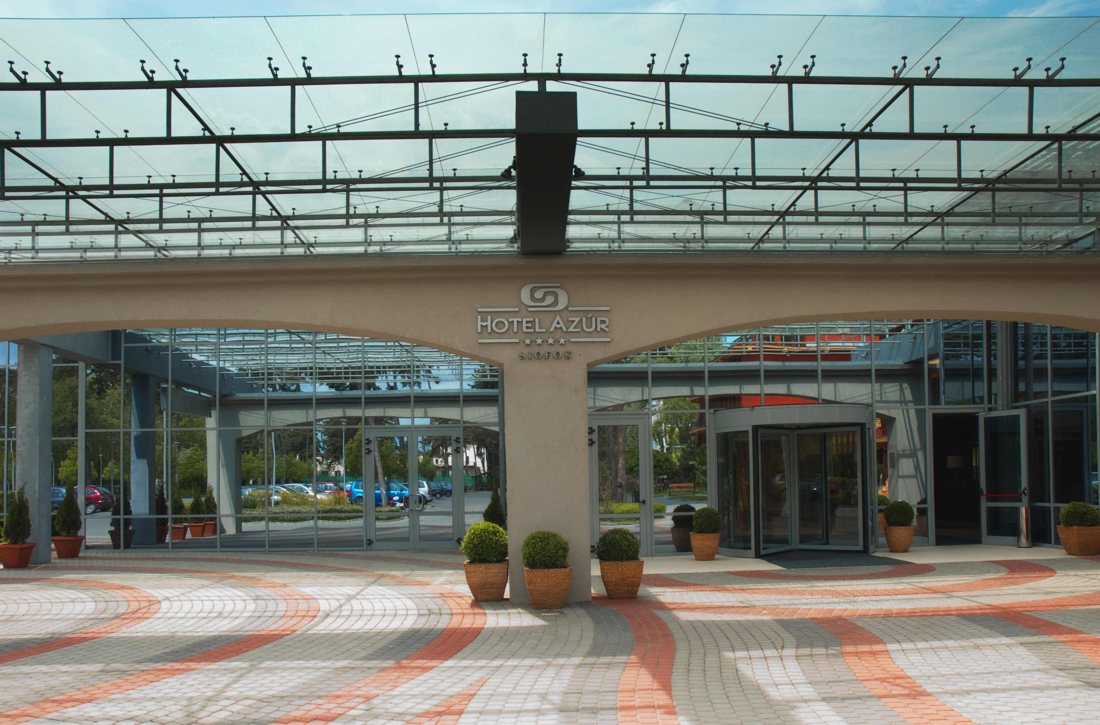 A modern hotel entrance with a glass facade, a covered walkway, and potted plants.