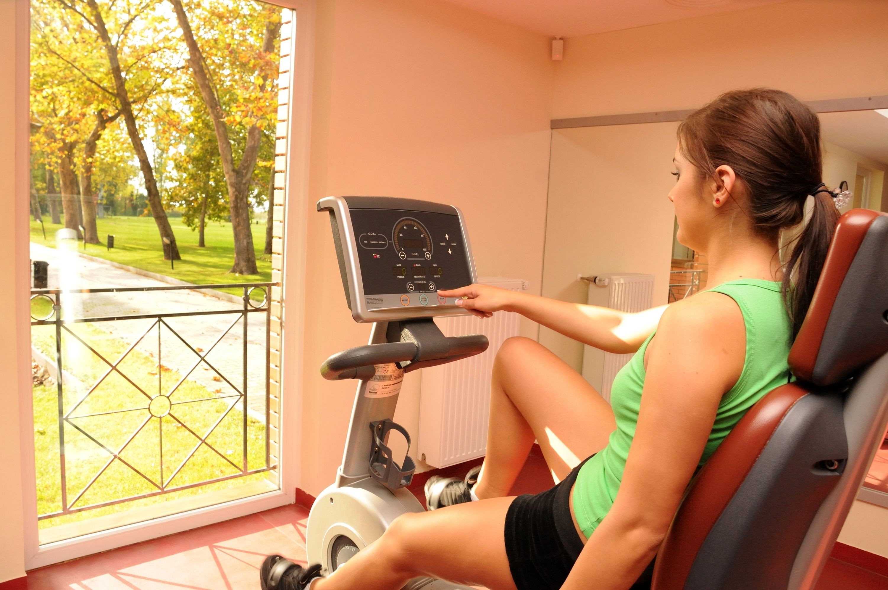 A woman using an exercise bike in a room with a view of a park.