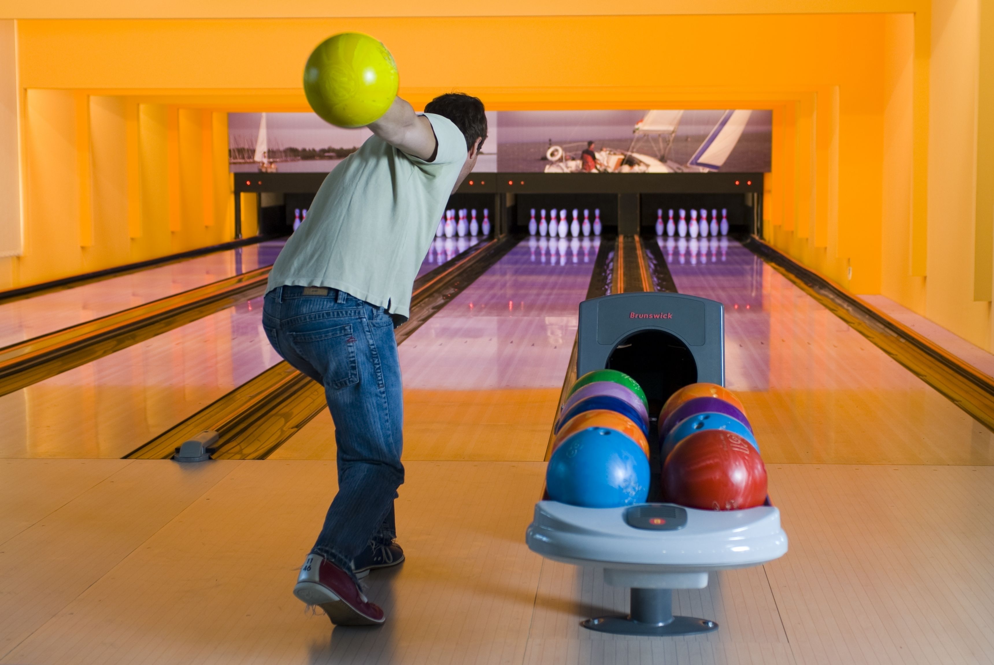A bowling alley with lanes, a bowling ball rack, and a bowling ball in motion.