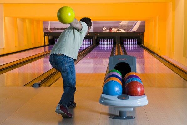Bolera con pistas, un porta bolas y una bola de bolos en movimiento.