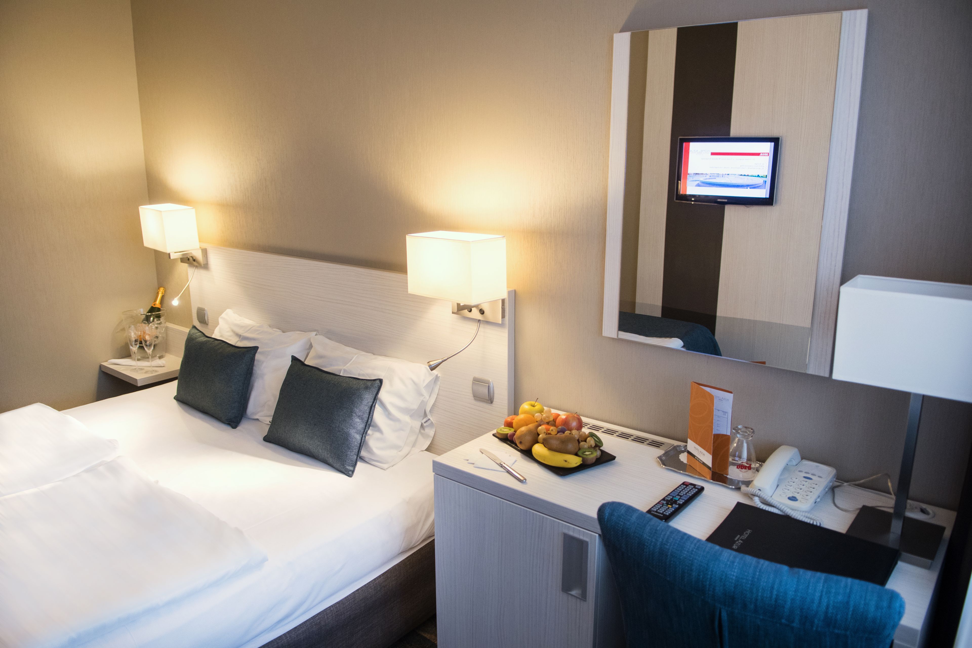 Een hotelkamer met een bed, nachtkastjes, een bureau met een fruitschaal, een telefoon, een afstandsbediening en een aan de muur bevestigde televisie.