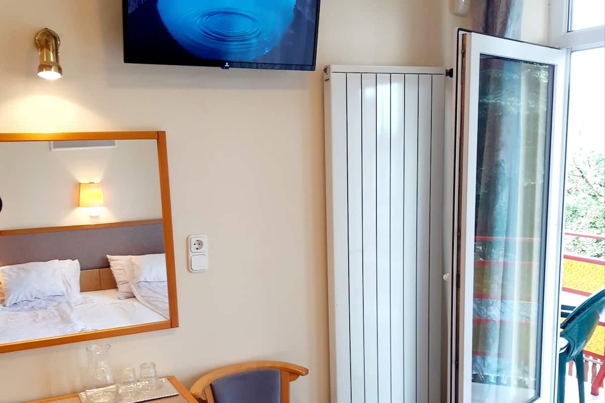 A hotel room with a bed, a desk with a chair, a television mounted on the wall, and a window with curtains.