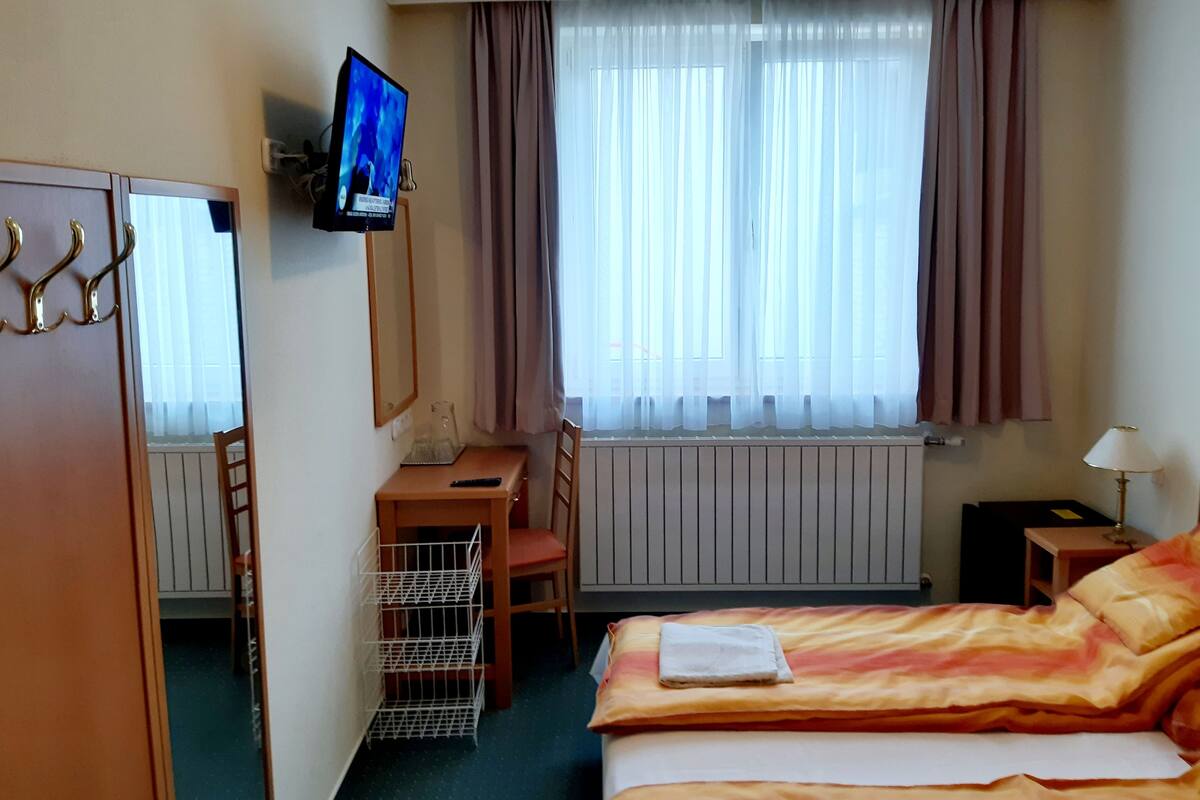 A hotel room with a bed, a desk, a chair, a television, and a window with curtains.