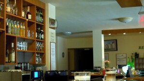 Un espace bar avec des étagères remplies de bouteilles et de verres, un comptoir de bar sur lequel se trouve une carafe de bière, et une machine à café.