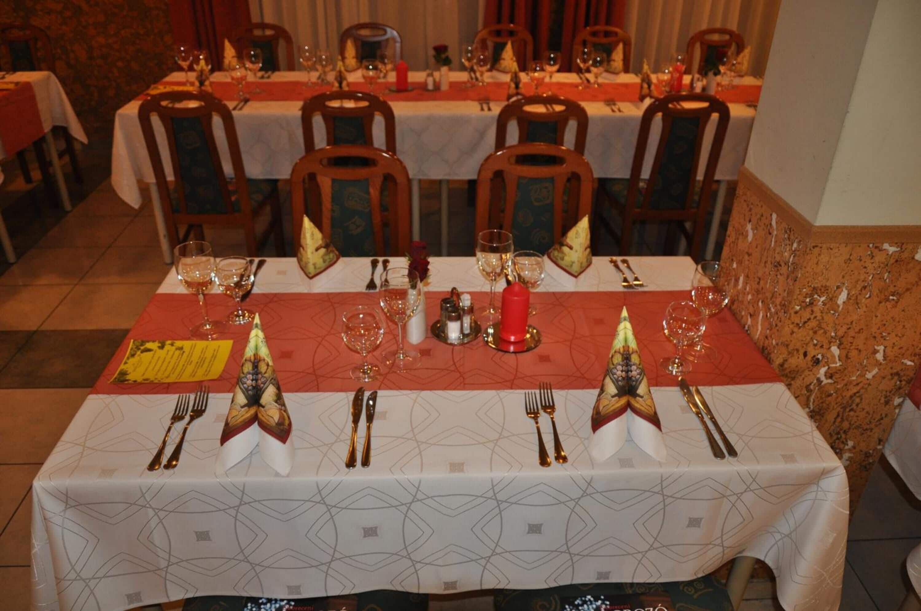 Zona de menjador amb taules preparades per a una posta, cadascuna amb un corredor de taula vermell, coberts daurats i vasos de vi.