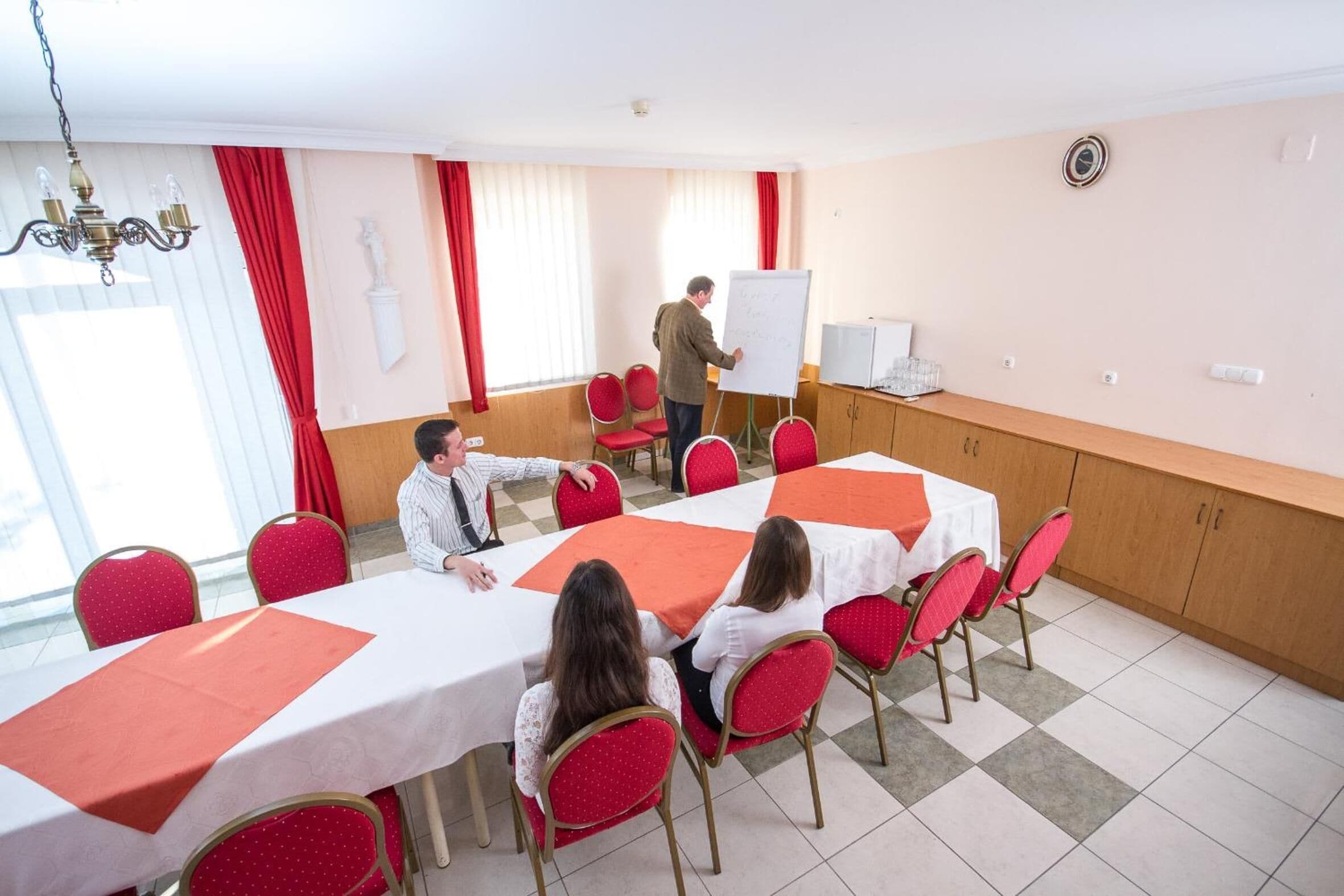 A conference room with a long table, red chairs, a whiteboard, and a chandelier.
