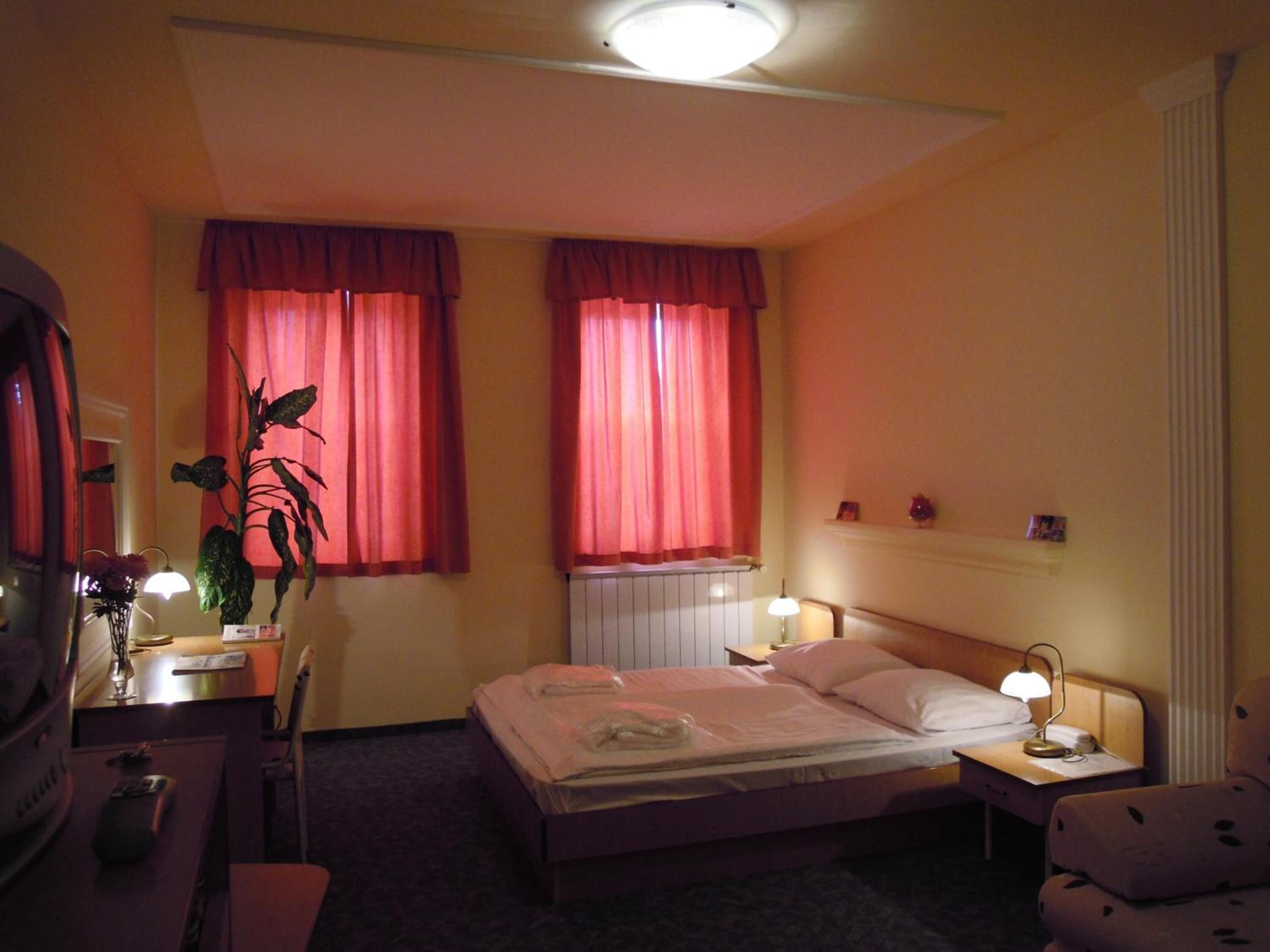 A hotel room with a bed, bedside tables, a desk, a chair, and a radiator.
