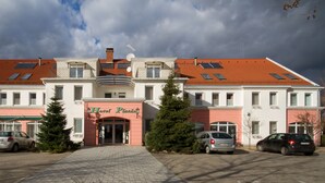 Un hôtel avec un toit recouvert de tuiles rouges, une entrée centrale dotée d’une porte en verre et des panneaux solaires sur le toit.