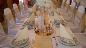 Une longue table de banquet, décorée de blanc et d’or, avec une composition florale centrale et des touches dorées sur les chaises et la vaisselle.