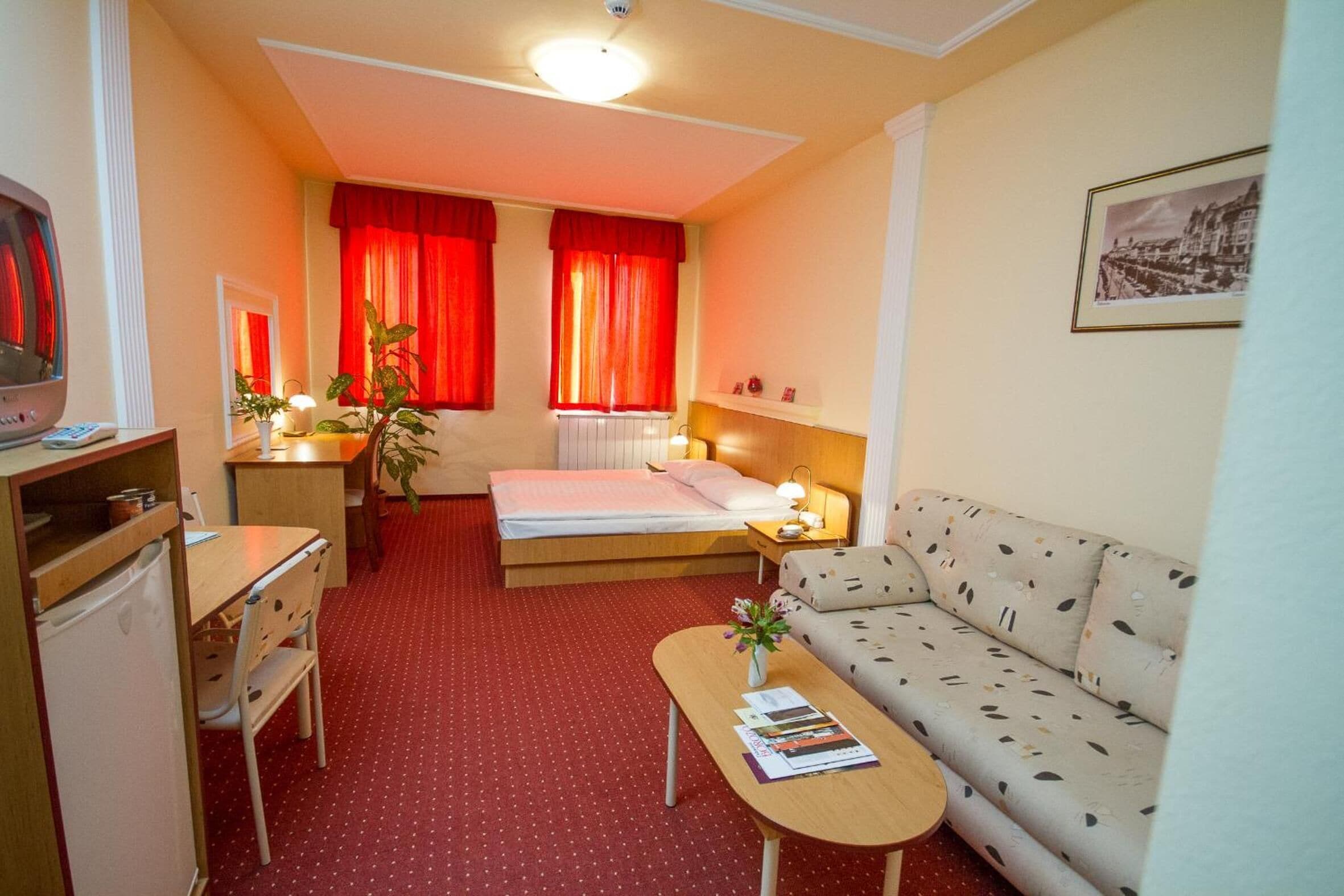 Una habitación de hotel compacta con cama, sofá, escritorio y una kitchenette pequeña.