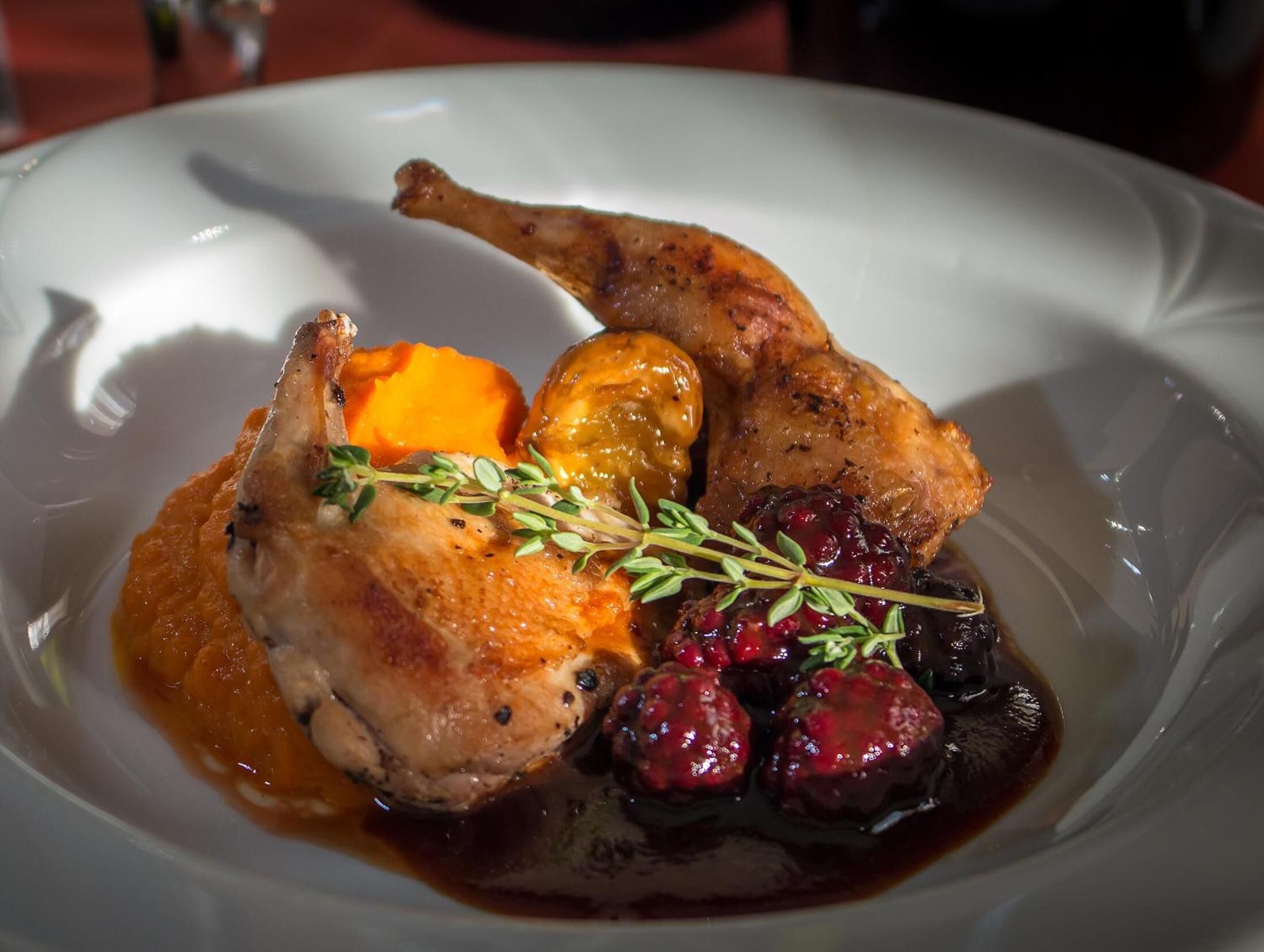 A plate with roasted duck, sweet potatoes, cranberries, and a sprig of thyme.