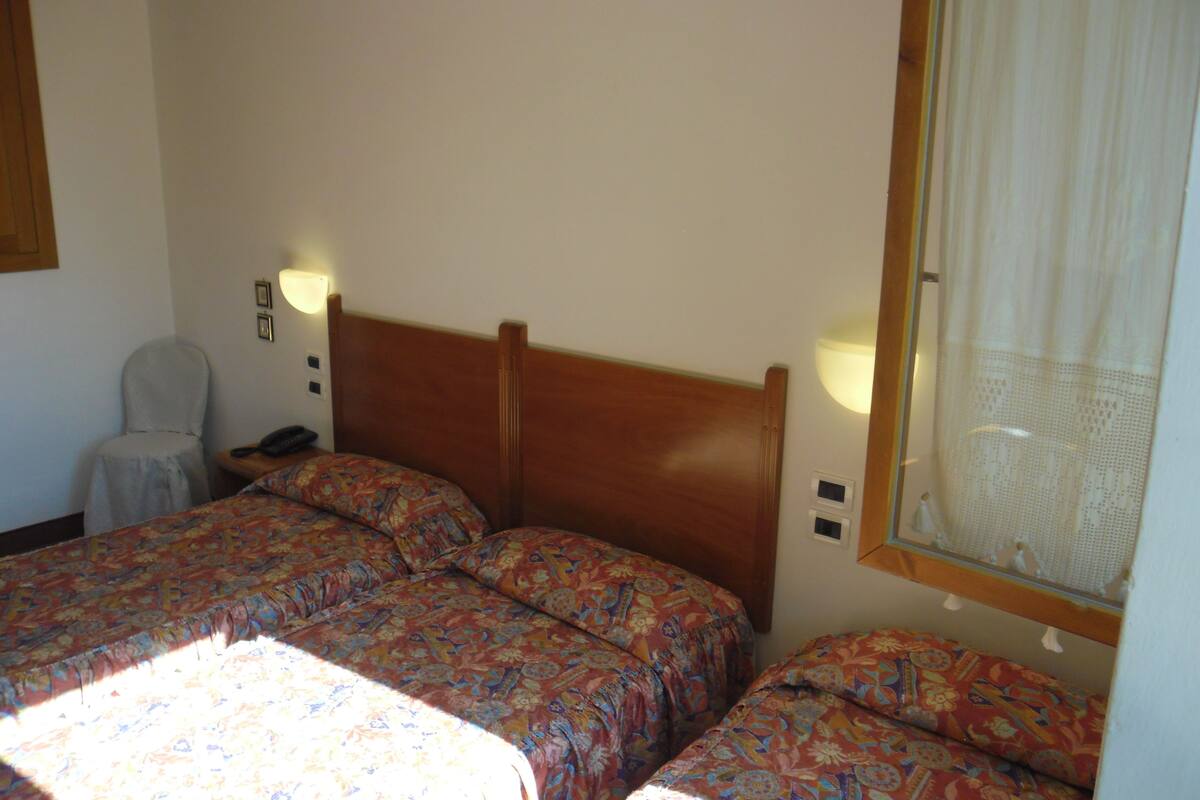 A room with two beds, a chair, a nightstand, and a window with a curtain.