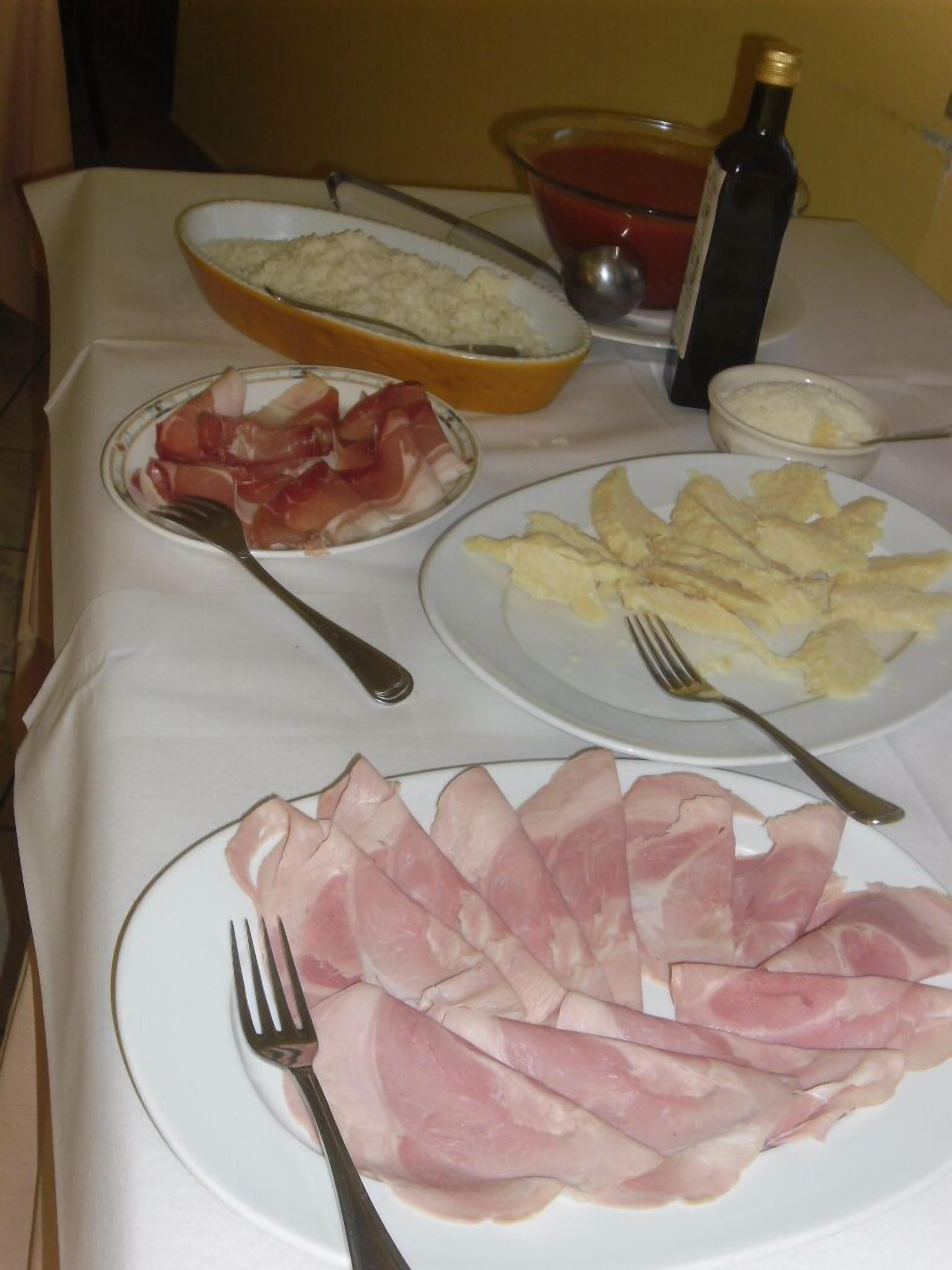 Une table avec des assiettes remplies de nourriture, notamment du jambon et des œufs, et une bouteille d’huile d’olive.