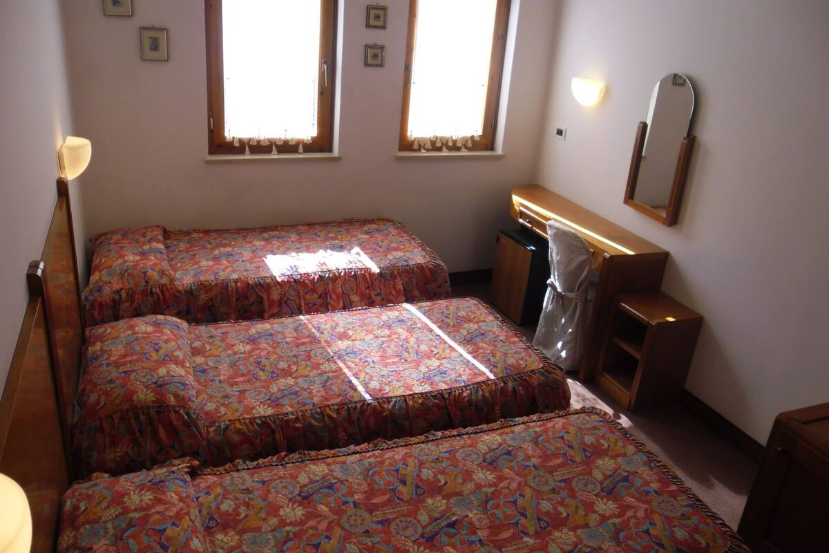 A room with two beds, a desk, a mirror, and two windows.