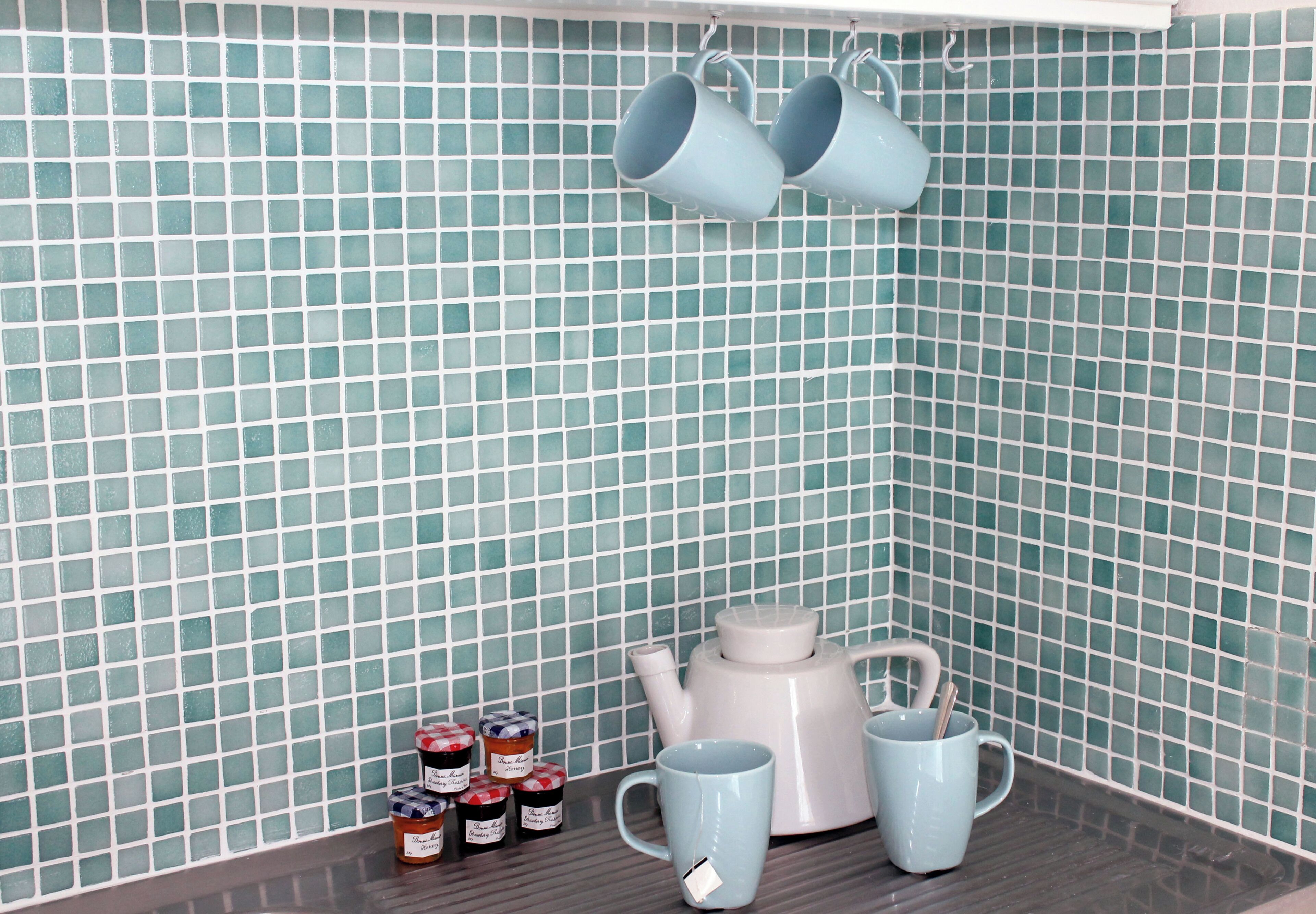 Un coin cuisine avec un mur recouvert de carreaux, une bouilloire, deux tasses et des pots contenant des condiments.