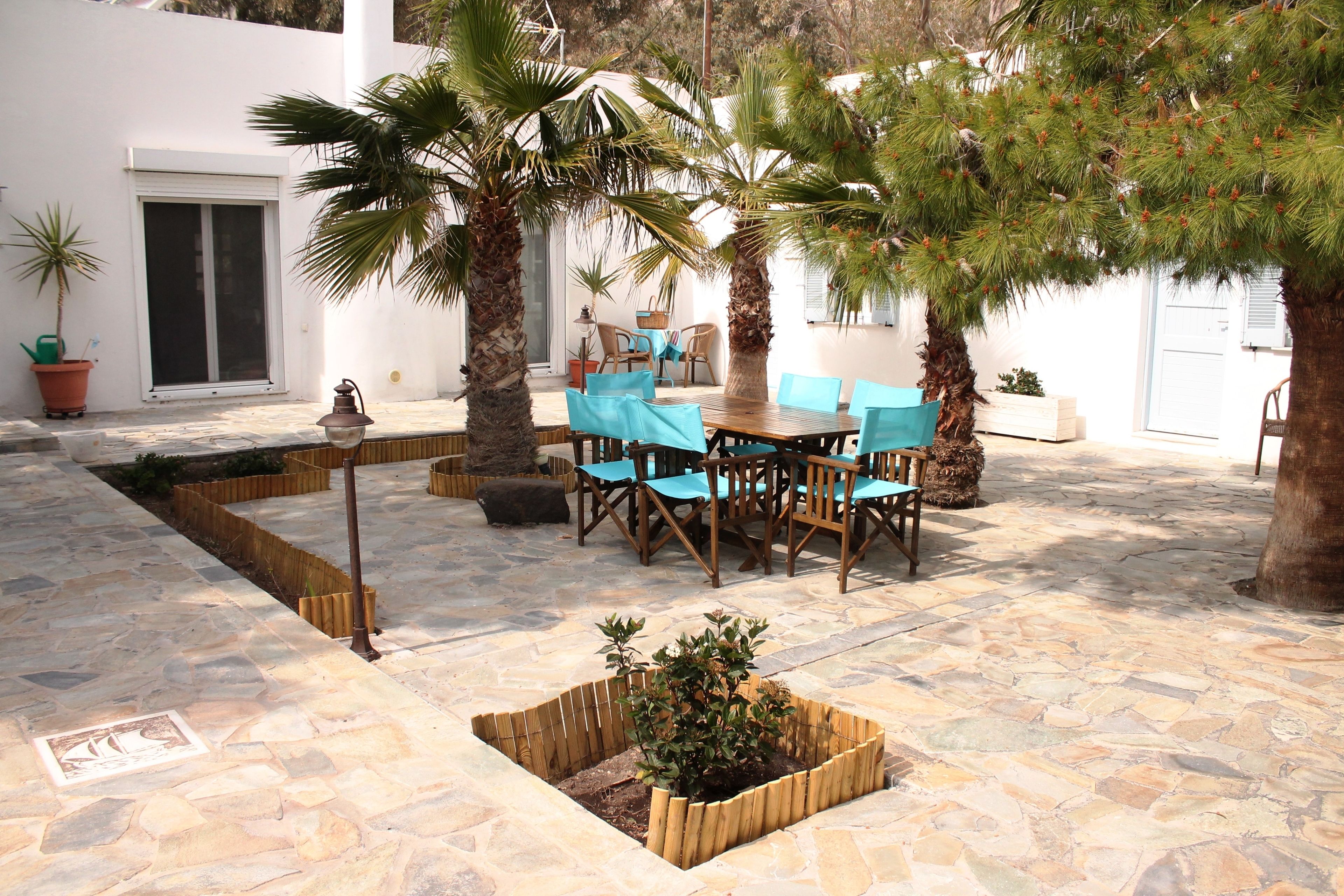An outdoor patio with stone flooring, wooden tables and chairs, and potted plants.
