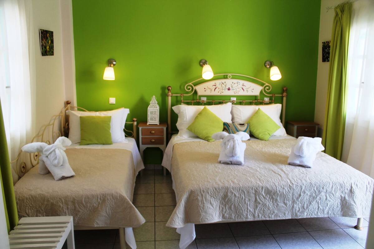 Quarto de hotel com duas camas, paredes verdes e roupa de cama branca.