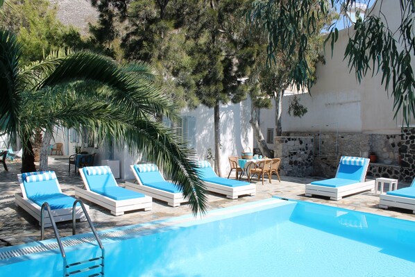 A poolside area with lounge chairs and a table, surrounded by trees and a stone wall.