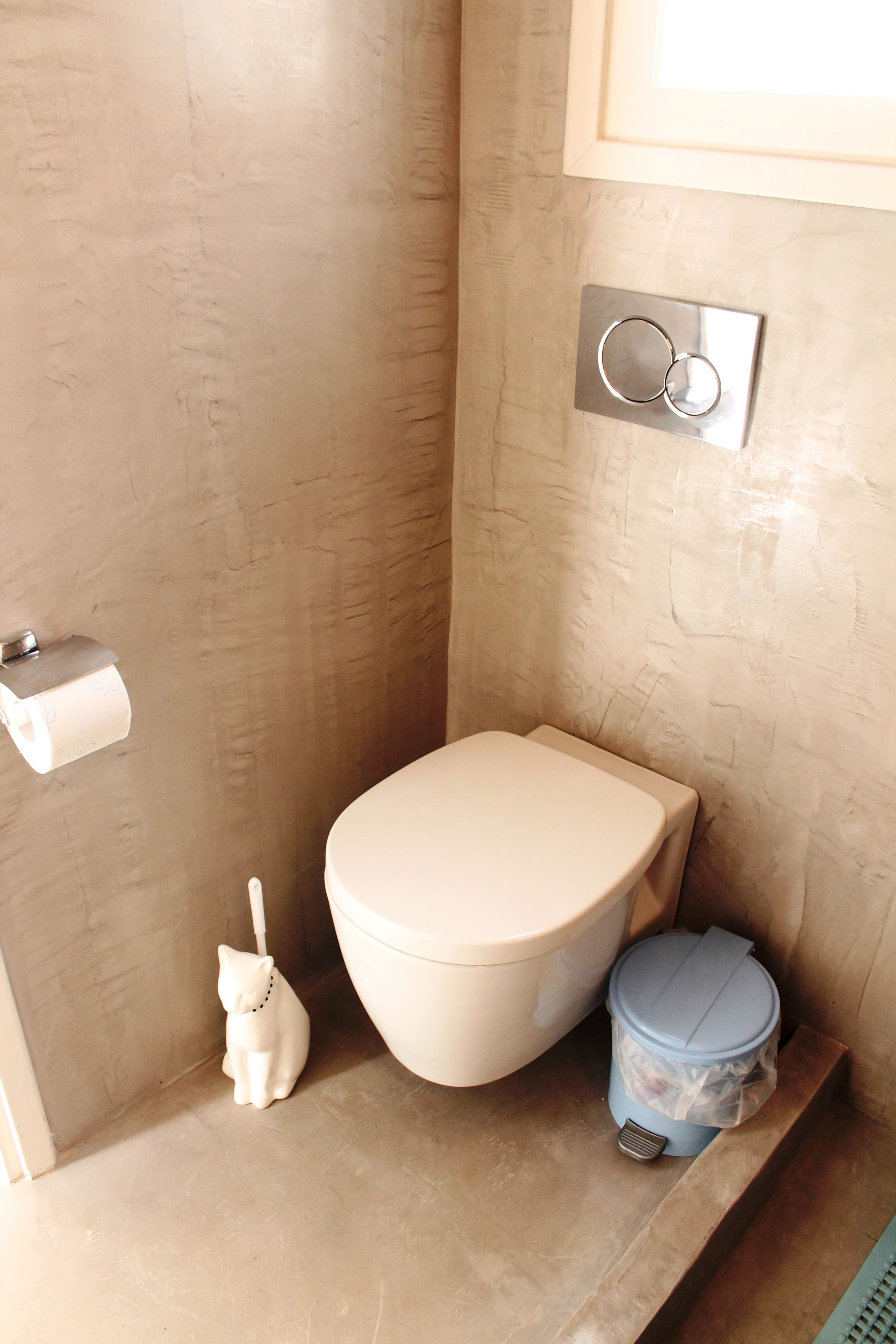 Un baño con inodoro, un pequeño cesto de basura y un dispensador de papel higiénico.