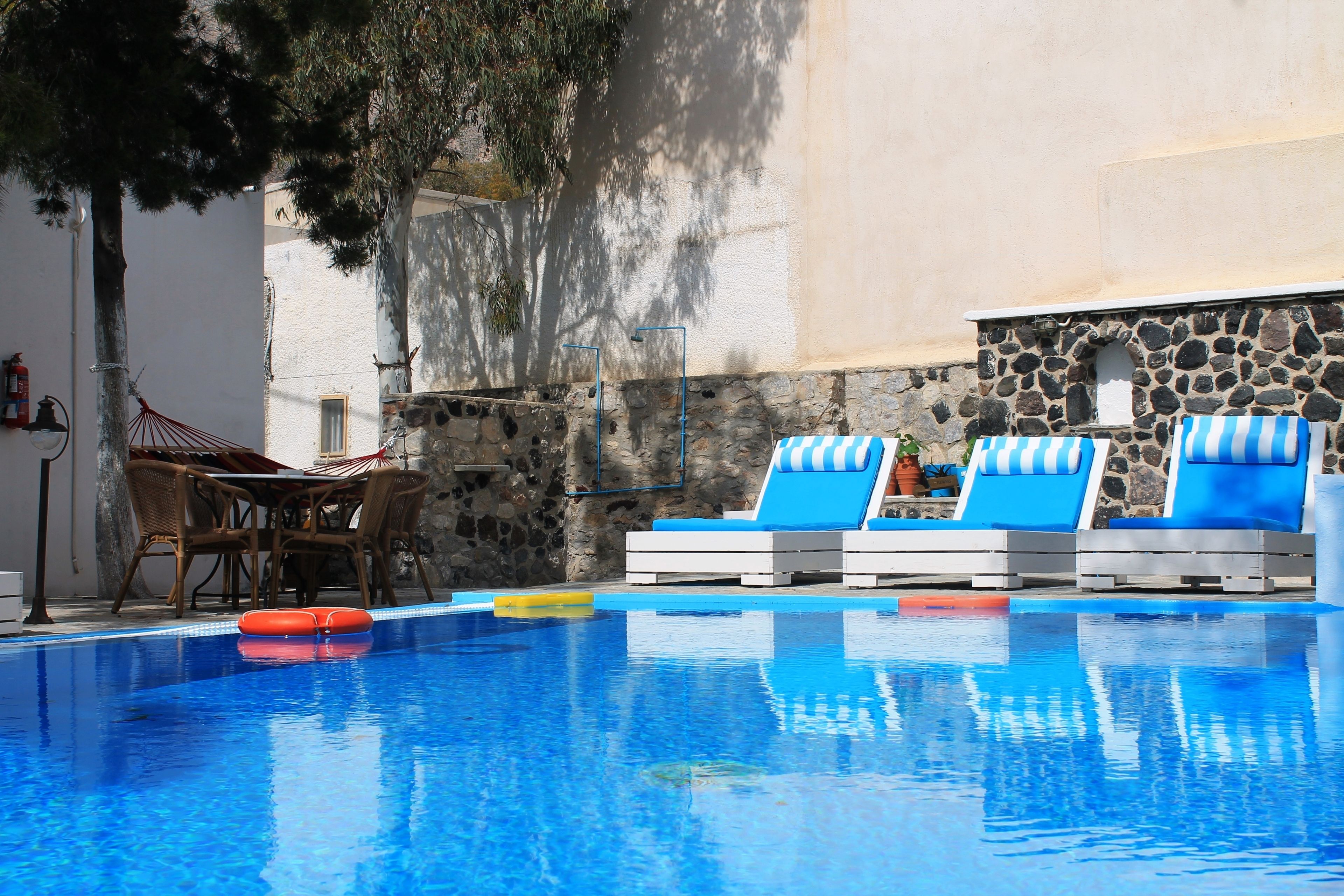 A swimming pool with lounge chairs and a table, surrounded by stone walls and trees.