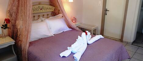 A neatly made bed with a purple bedspread, a canopy, and a bouquet of white towels.