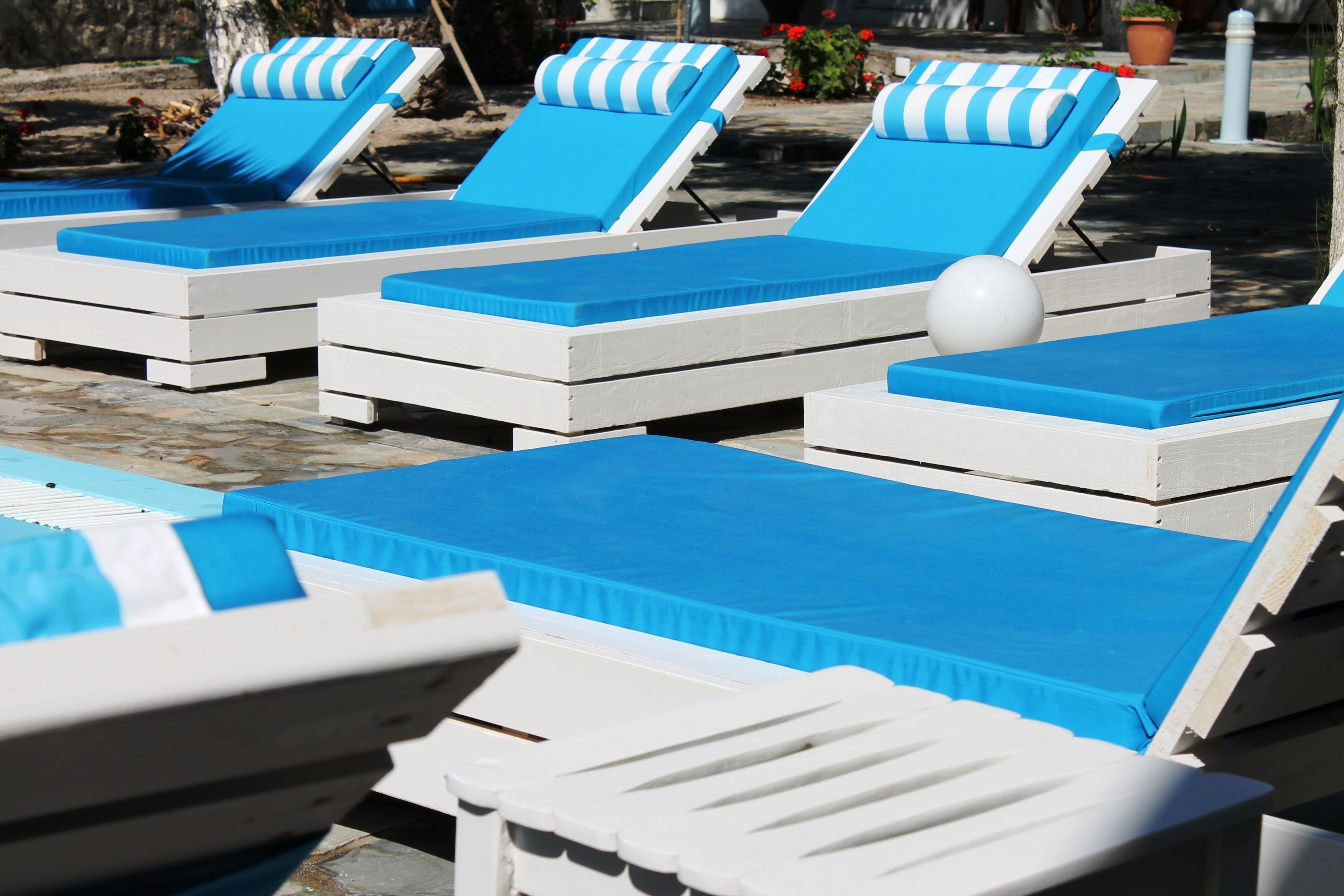 Una fila de sillas reclinables blancas con cojines azules y un mantel azul, dispuestas alrededor de una piscina.