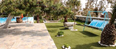 A stone pathway leading to a pool area with a swing set and palm trees.