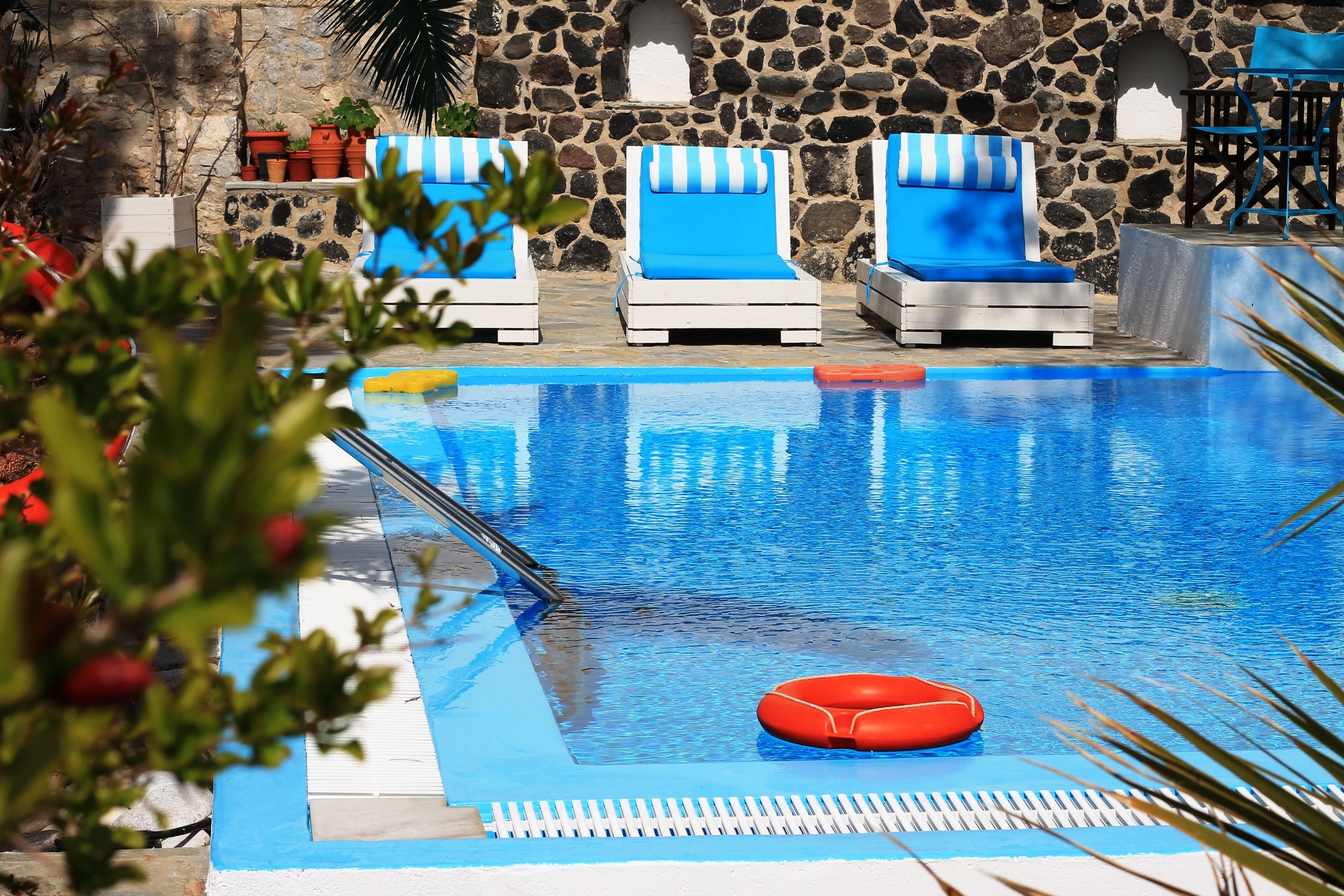 A swimming pool with blue and white striped lounge chairs, a stone wall, and potted plants.